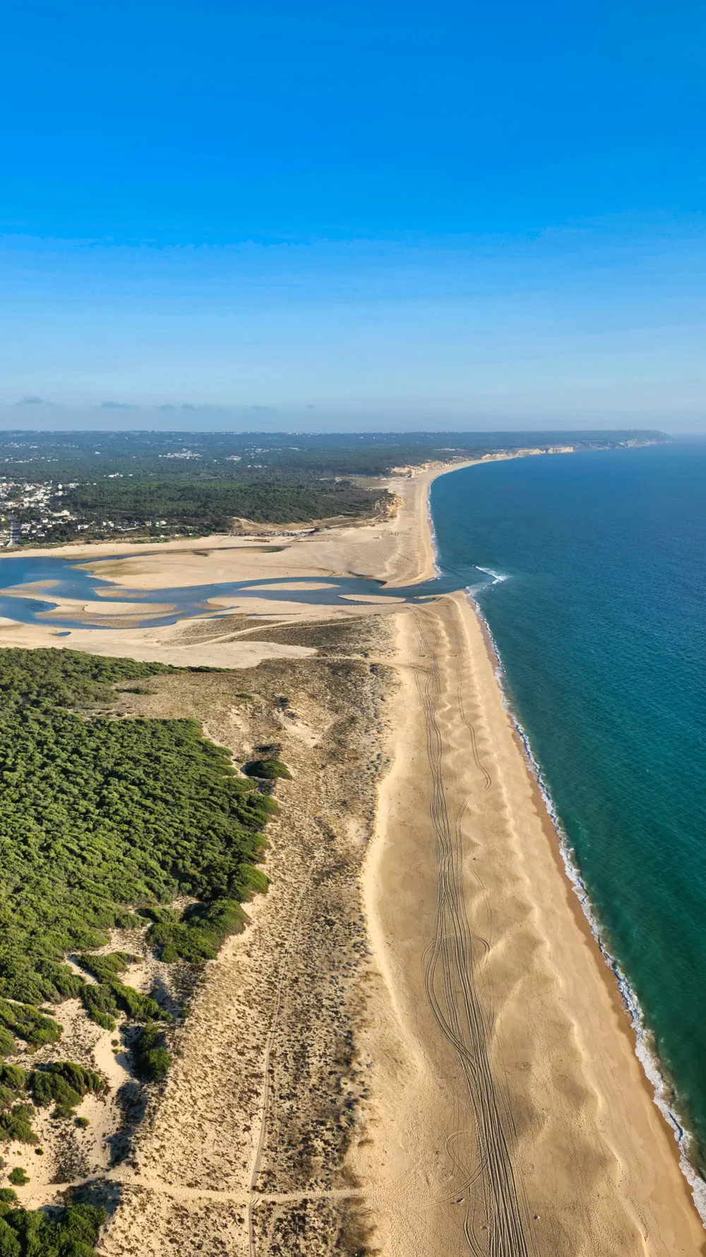 Vista aérea de la Lagoa de Albufeira: la laguna con bancos de arena a la izquierda, el pinar, la playa extensa y el mar abierto a la derecha.